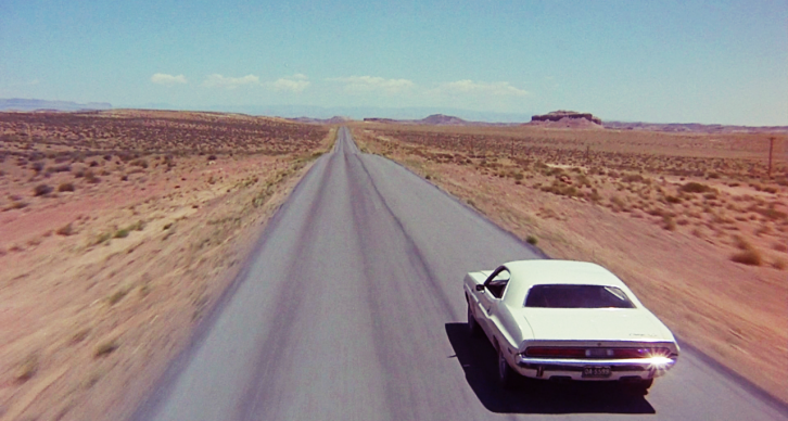 Old car driving along road through the desert