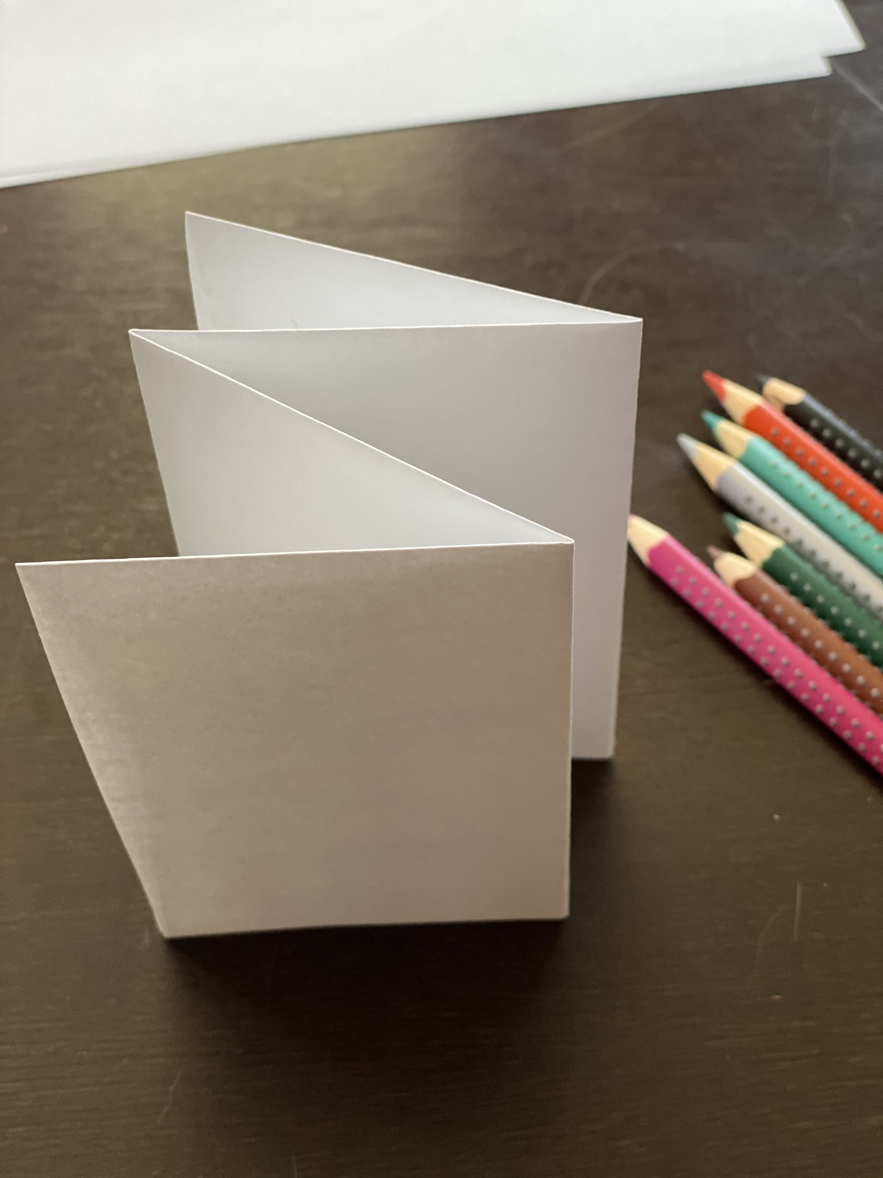 Folded paper standing on its edges, with colored pencils to the side