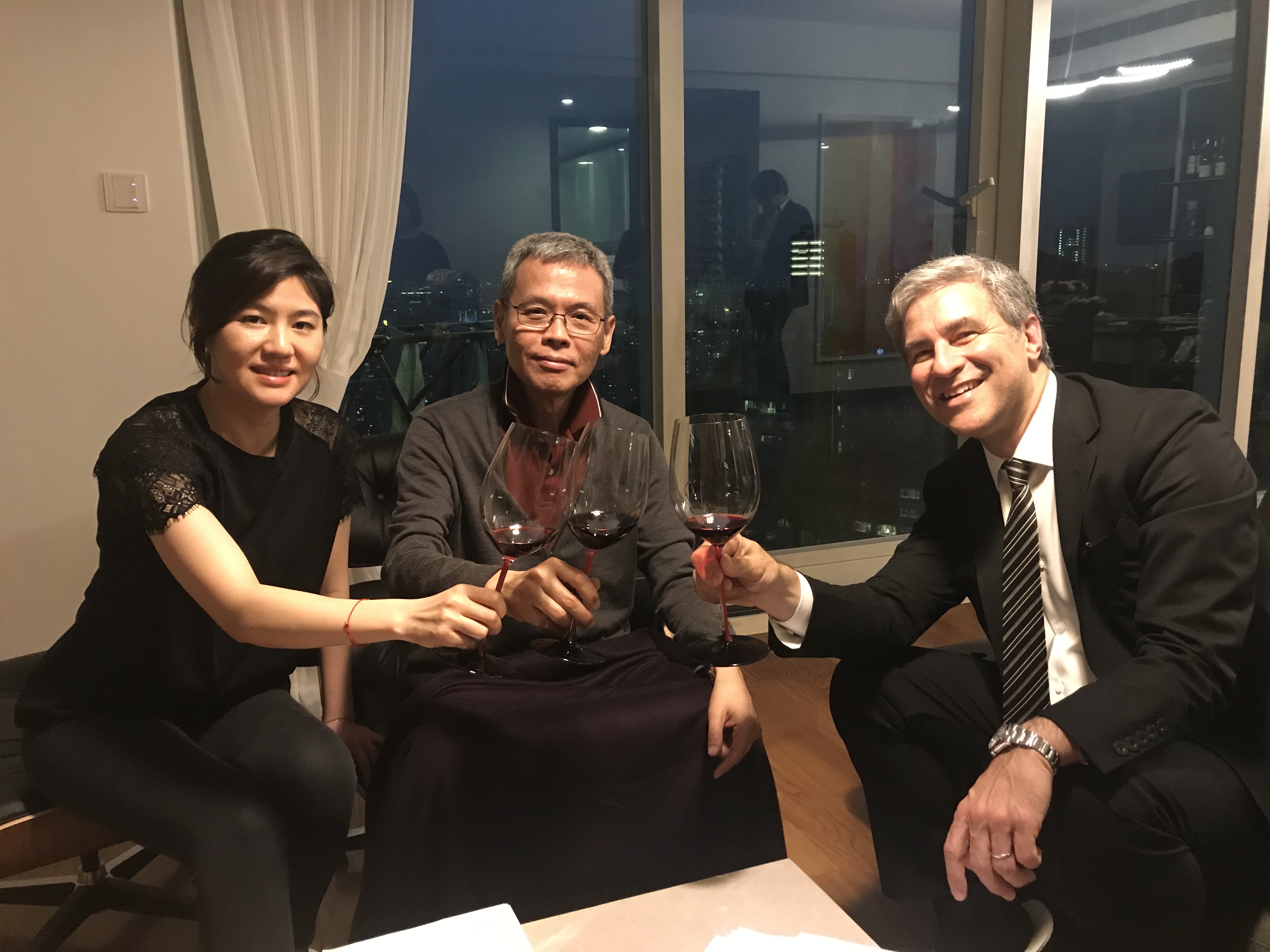 Three people sitting and holding glasses of wine in a room with large windows behind them