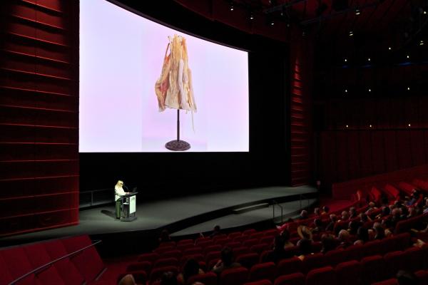 Presenter onstage with artwork on a large screen in a theater