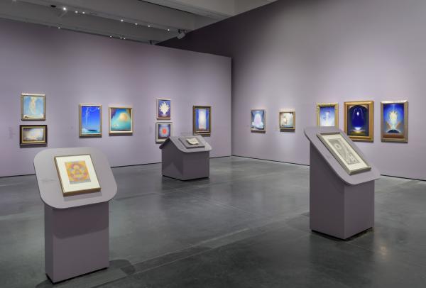 Gallery view with paintings on lavender walls and podiums