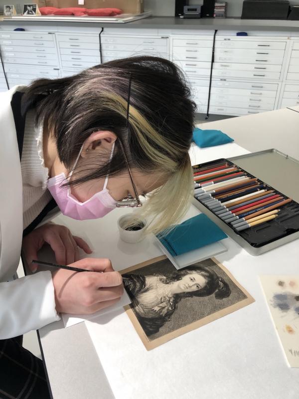 Conservation intern painting a black and white print of a woman