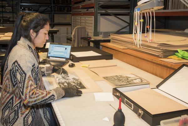 woman sitting at a table, wearing gloves, preparing photographs to be stored