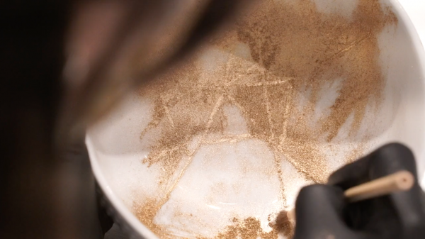 Close-up of gold dust being brushed onto the filled-in cracks of a white bowl