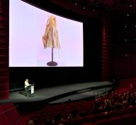 Presenter onstage with artwork on a large screen in a theater