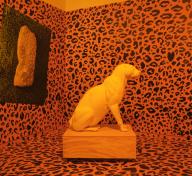 installation of room with orange and black leopard print walls and floor with a white leopard statue in the center