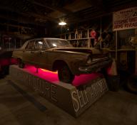 Installation of Michael C. McMillen's Central Meridian, a dark, workshop-like space featuring a vintage car