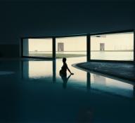 Pregnant woman standing in waist-deep indoor pool, lit in silhouette