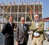 Three men stand in front of a three story building under construction