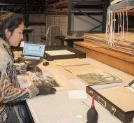 woman sitting at a table, wearing gloves, preparing photographs to be stored