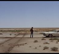 Man standing next to old car on desert road